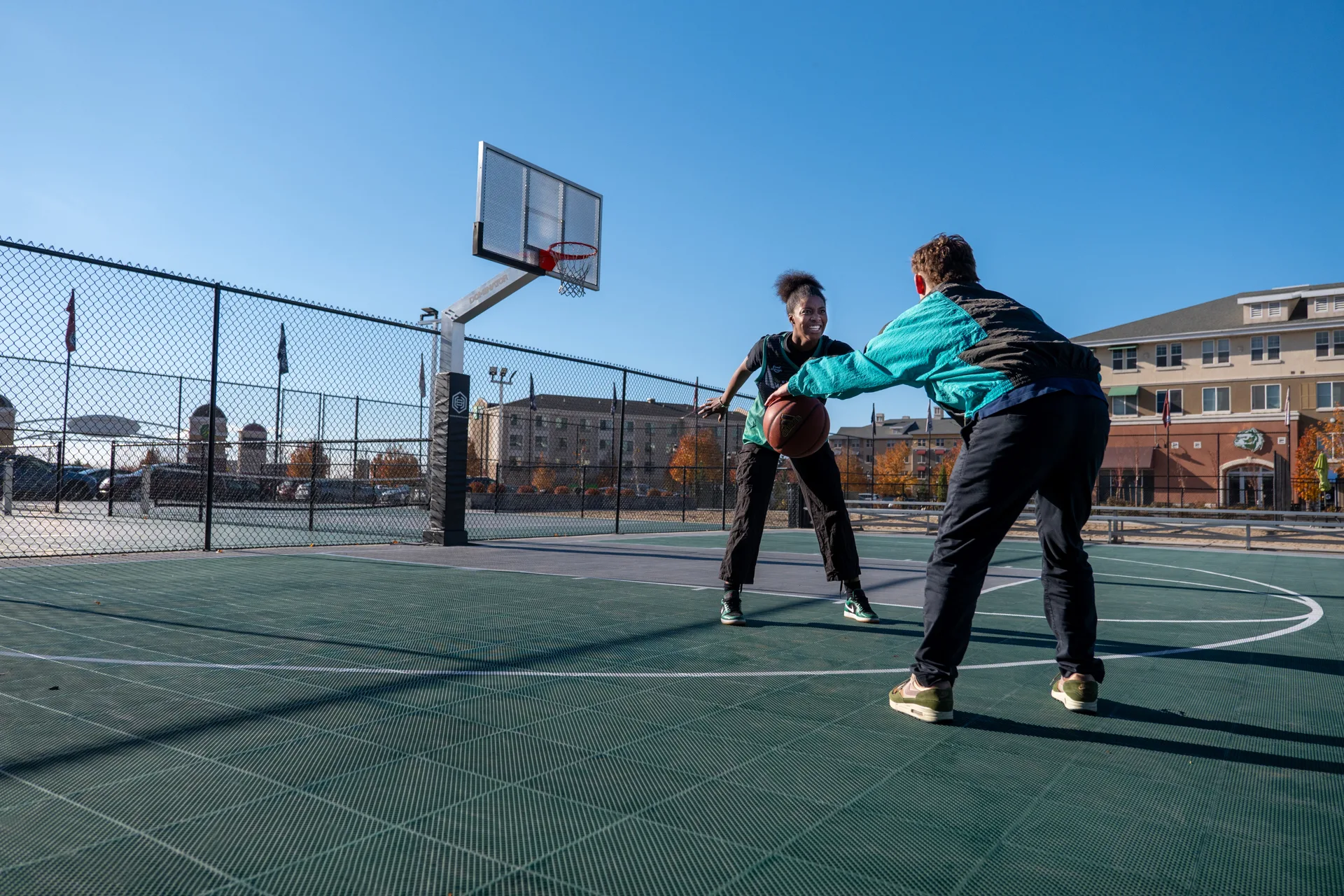 Two basketball players in the middle of a game on a facility's outdoor basketball court