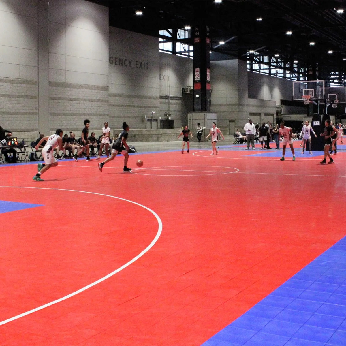 Groups of kids playing a basketball game on a red and blue indoor basketball court
