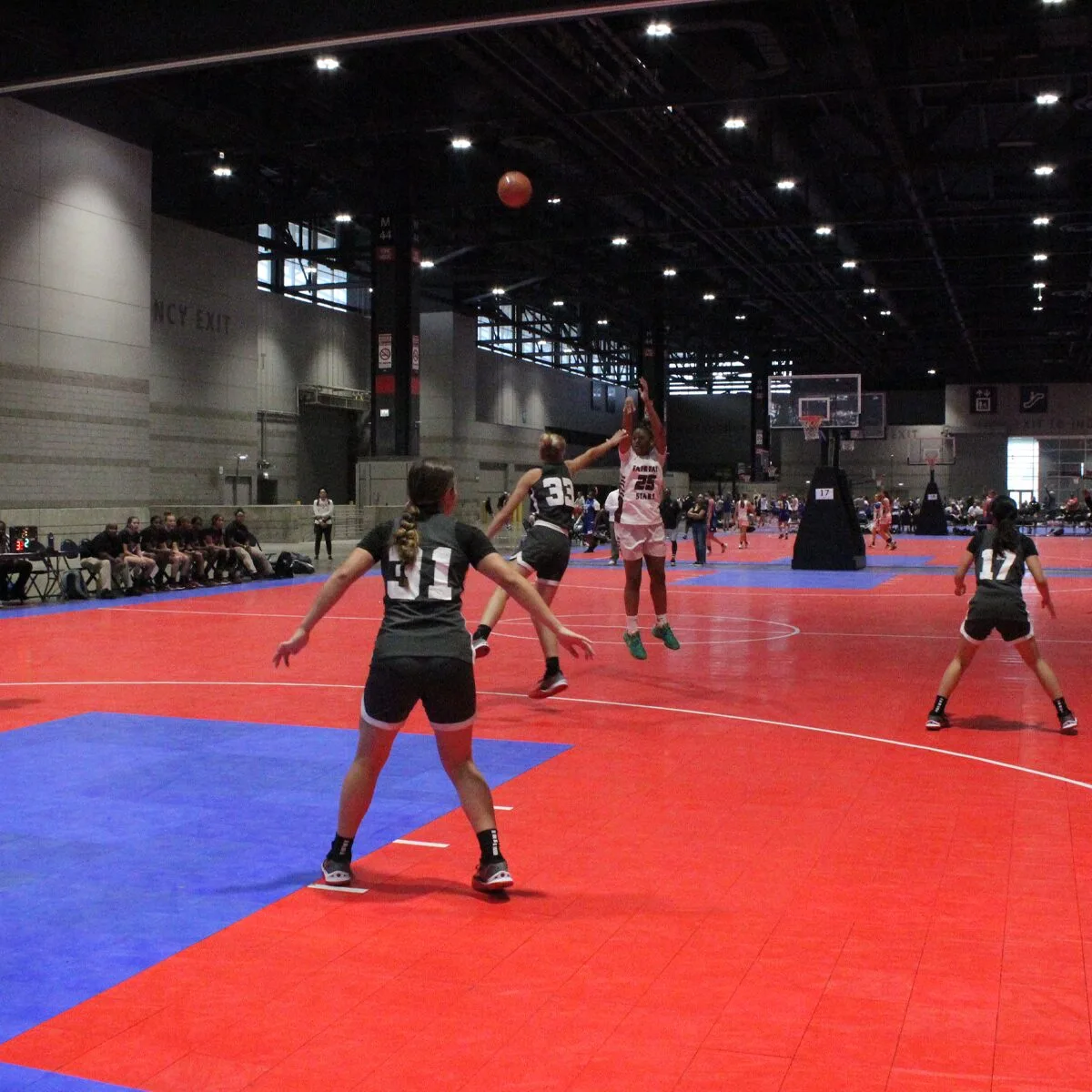 Girls playing a competitive indoor basketball game on red and blue court flooring